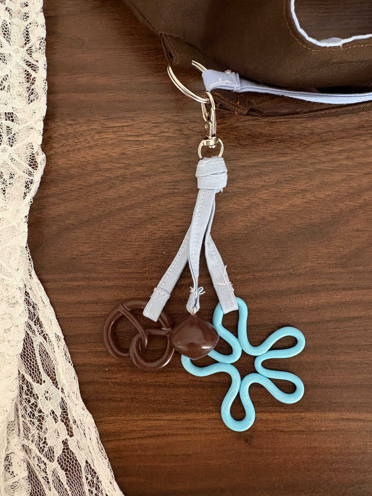 bijou de sac bleu en tissu bleu avec des breloques en forme de fleur bleu, bretzel marron et pierre marron accroché à un sac à main
