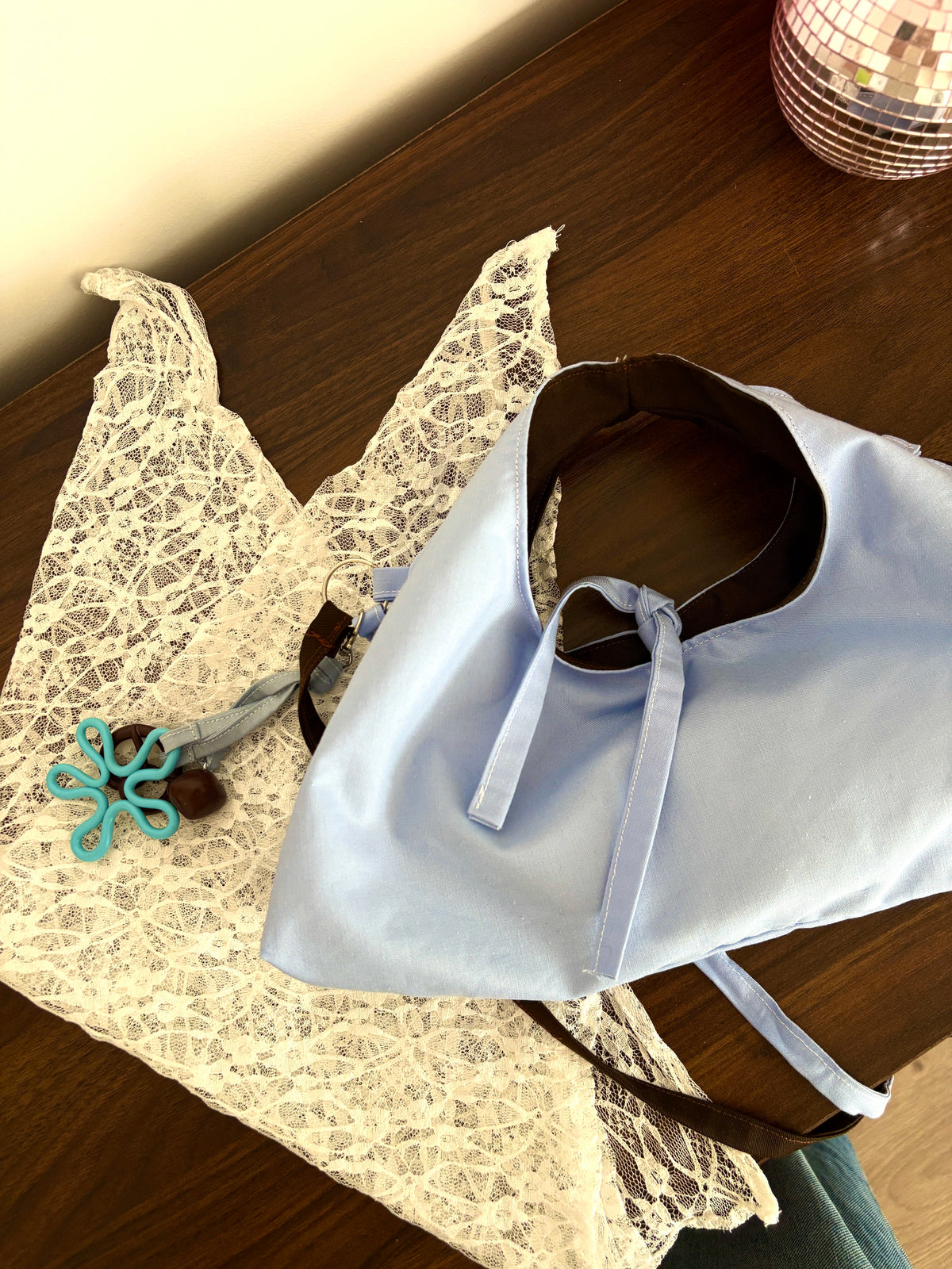 lot cinnamon avec le sec réversible face bleue, le bandana en dentelle plié et le bijou de sac marron et bleu accroché au sac, le tout posé sur une table en bois