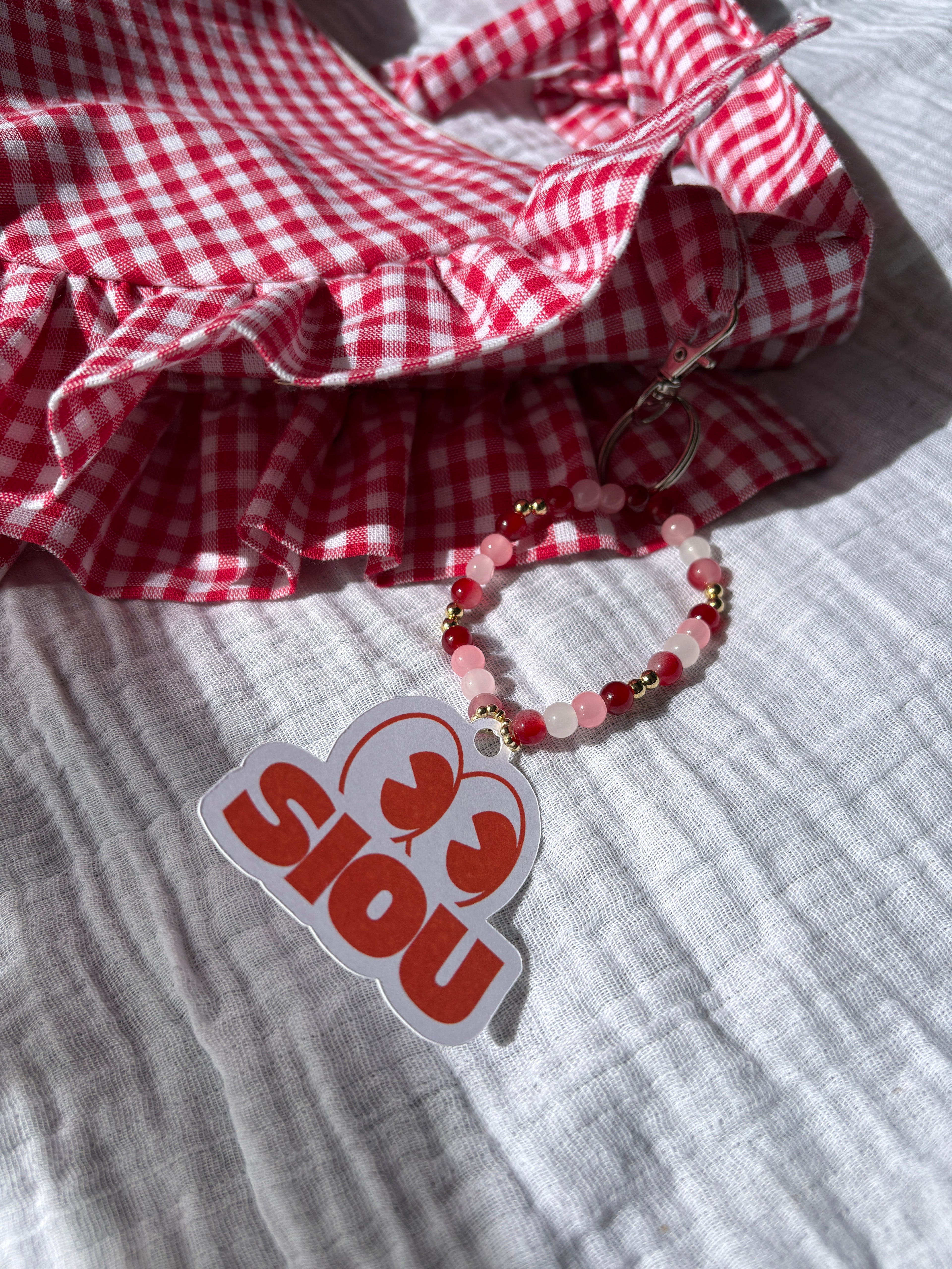 Bijou de sac en perles en verre rouge, rose et blanc du sac à main à volants en forme de demi-lune/croissant de la marque SIOU, cousu main, coloris Fraise, collection Printemps, sur une nappe en gaze de coton
