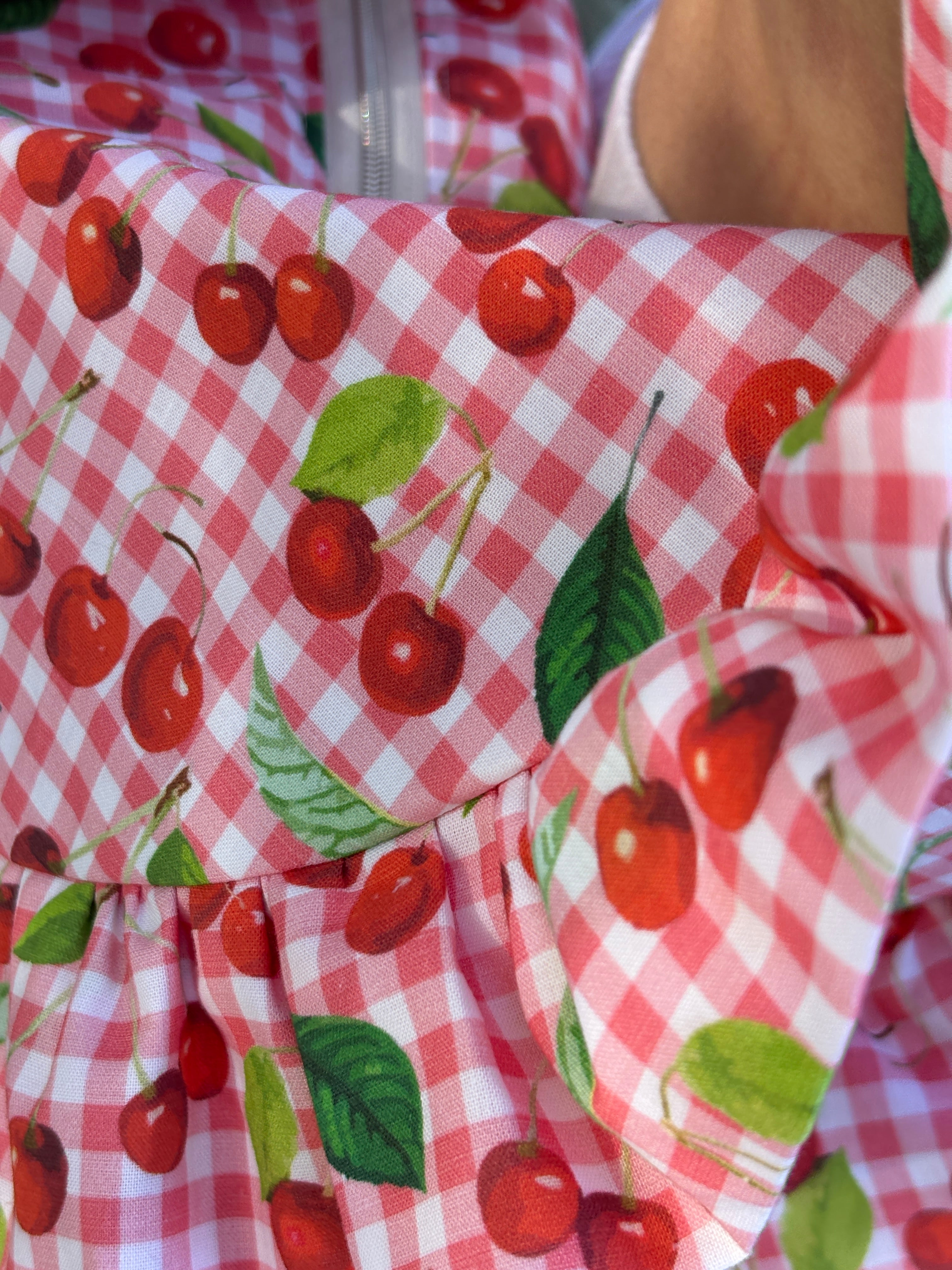 Zoom sur le tissu du sac à main cousu main en forme de demi-lune à froufrous Cerise, le motif est composé de cerises sur un fond vichy rouge et blanc.