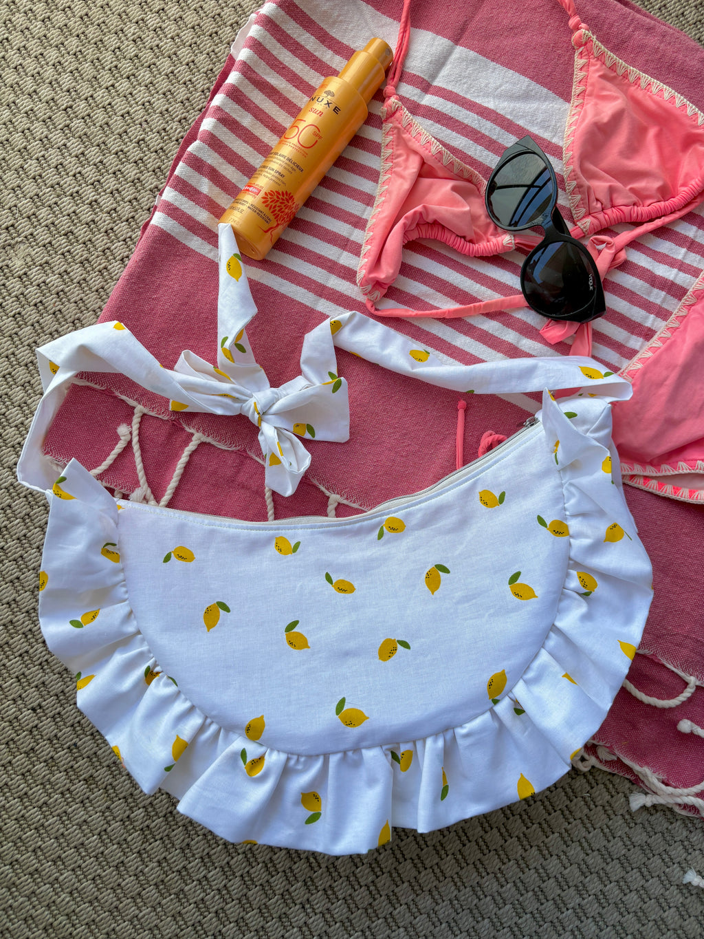 Sac à main en tissu à volants en forme de demi-lune/croissant, cousu main, coloris mini citrons sur fond blanc, collection
Été, sur une serviette de plage, sur du sable avec un bikini, un tube de crème solaire et des lunettes de soleil autour.