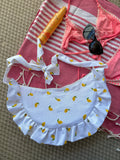 Sac à main en tissu à volants en forme de demi-lune/croissant, cousu main, coloris mini citrons sur fond blanc, collection
Été, sur une serviette de plage, sur du sable avec un bikini, un tube de crème solaire et des lunettes de soleil autour.