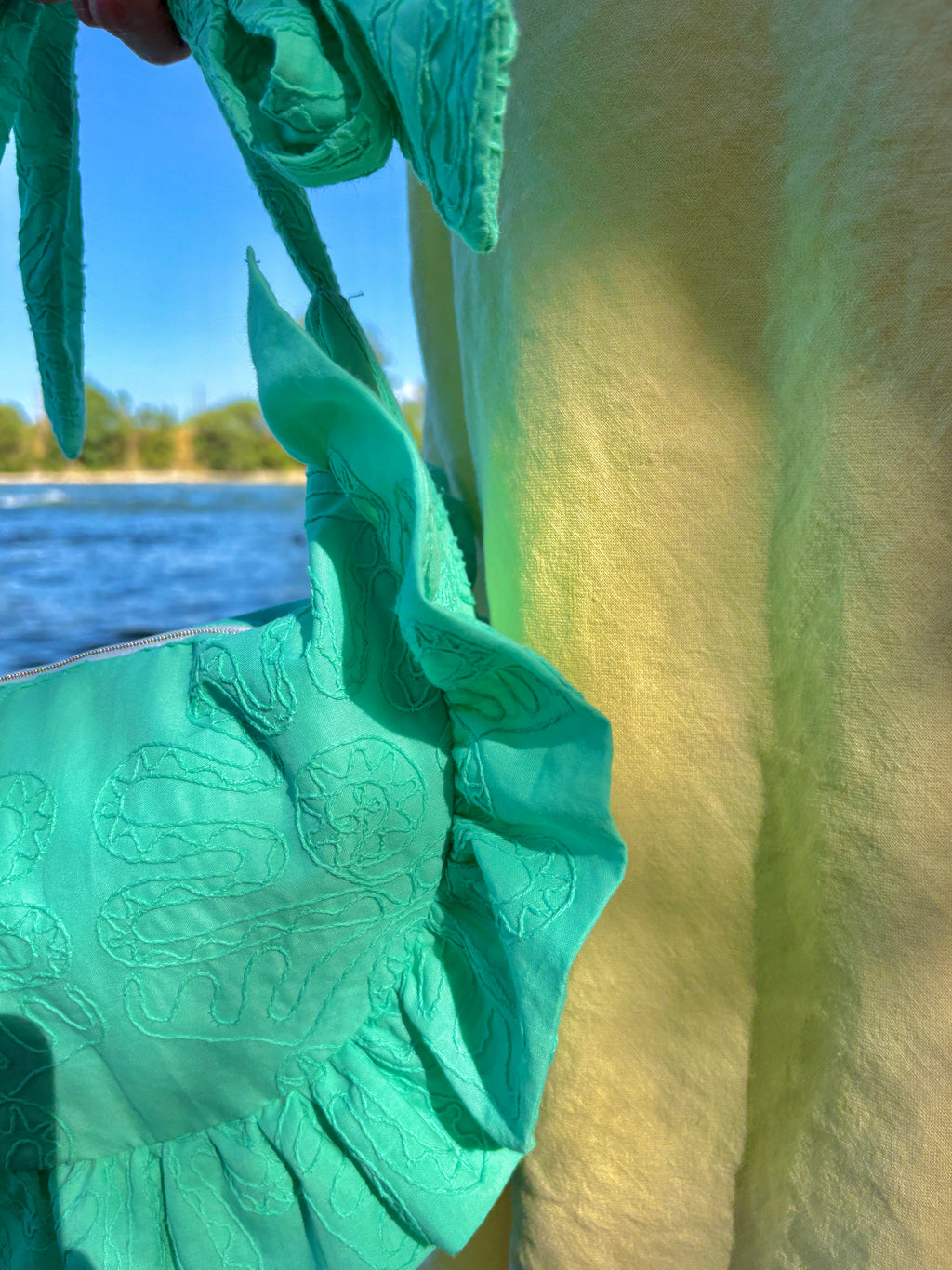 Zoom sur les détails de couture du sac à main à volants en forme de demi-lune SIOU, au coloris Lagon, une couleur turquoise vive qui est mis en valeur par des broderies organiques.