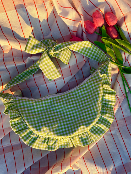 Sac à main en tissu à volants en forme de demi-lune/croissant, cousu main, coloris en vichy vert et blanc Basilic, collection Printemps, sur une nappe de pique-nique, sur de l'herbe avec des tulipes autour du sac de la marque SIOU
