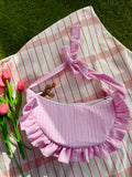 Sac à main en tissu gaze de coton à volants en forme de croissant, cousu main, coloris rayures rose et blanc Tulipe, collection Printemps, sur une nappe de pique-nique, sur de l'herbe avec des tulipes autour du sac de la marque SIOU